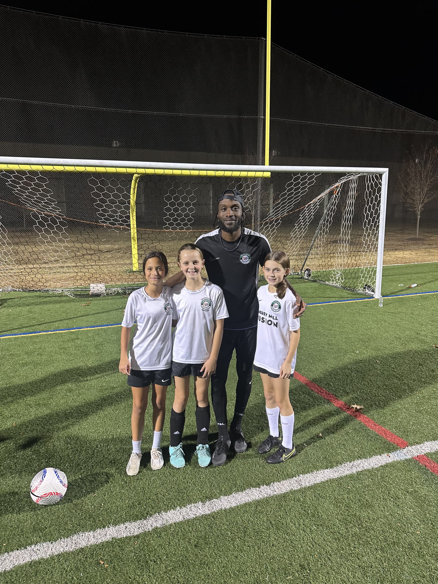 CJ Sapong with three young players in front of a goal after an evening training session.