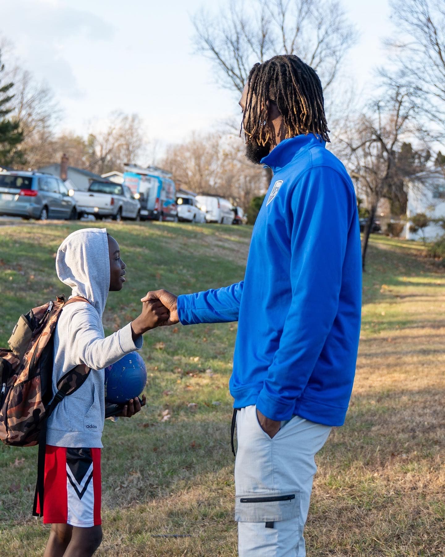 CJ Sapong greeting a young player with a handshake beside a pitch.