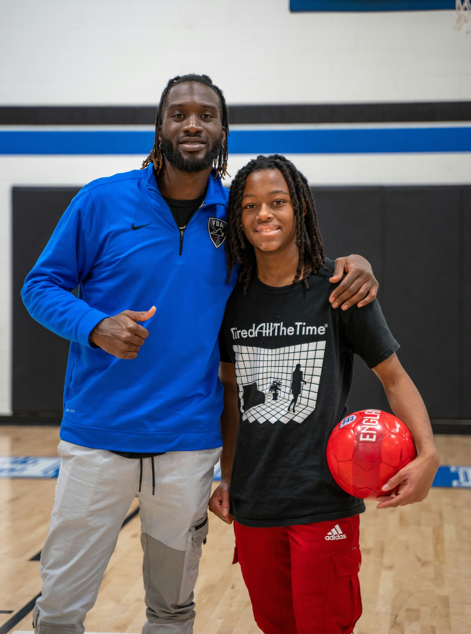 CJ Sapong with a young player holding a ball, standing together in a gym.